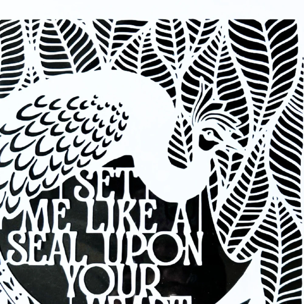 The peacock in the middle of the white papercut is surrounded by broad leaves. The English text for the quote sits between the peacock's curved tail and body.