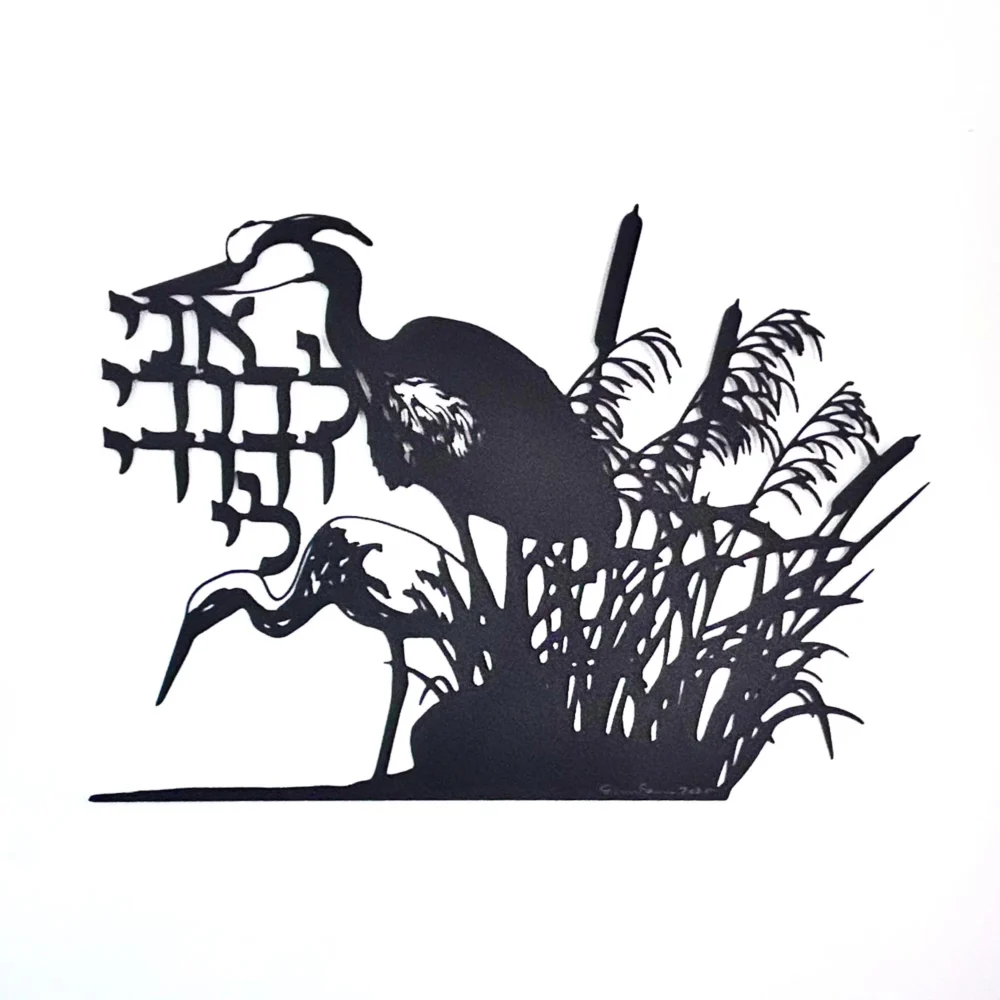 Black papercut art piece depicting two herons in a marsh setting with cattails and reeds. The artwork includes Hebrew text and is set against a white background. The herons are in silhouette.