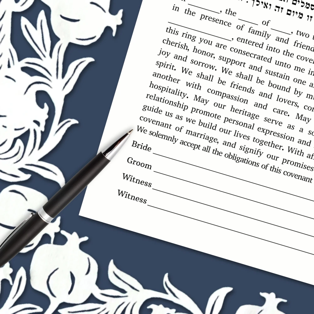 close up of white and blue papercut ketubah with pomegranates, and a pin laying across the text, ready to sign