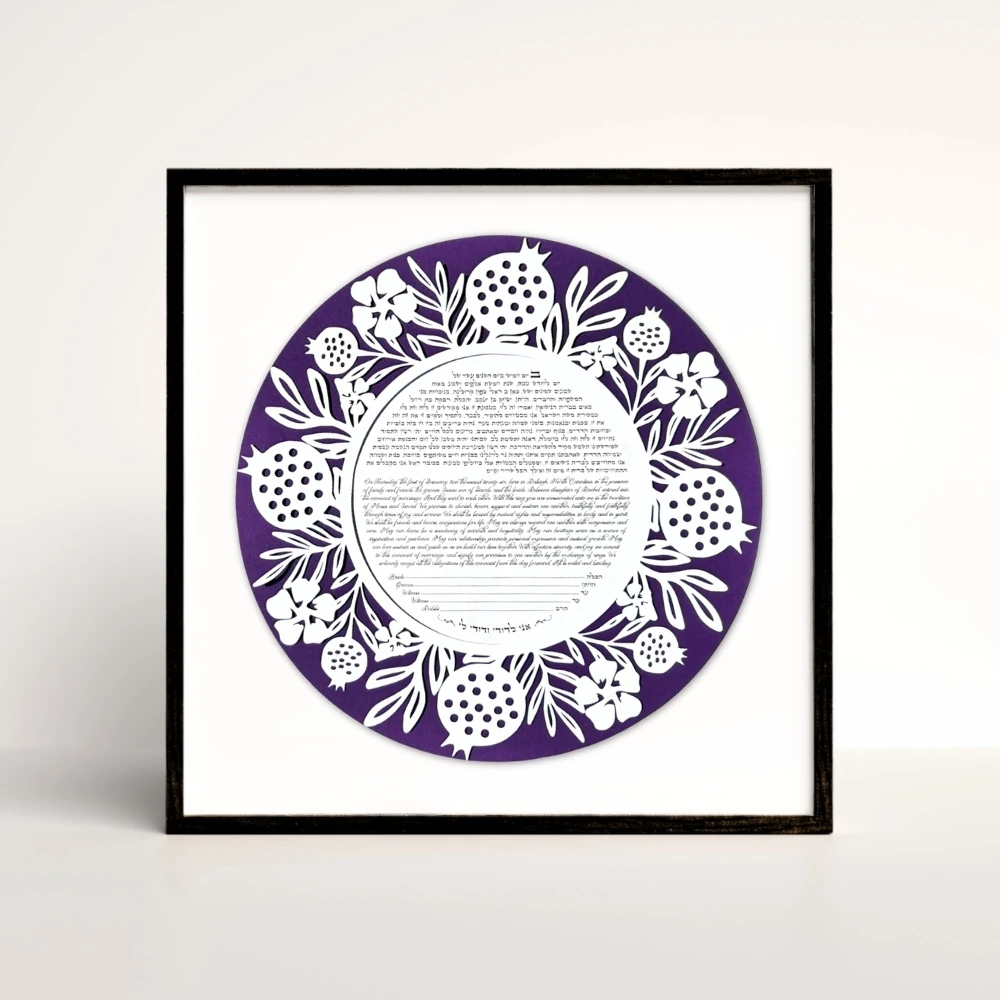 Purple papercut pomegranate and floral ketubah in a black frame.